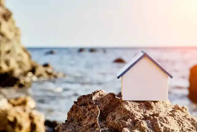 Miniature house model on rocky shore representing beachfront real estate and vacation rentals along Florida’s Space Coast.