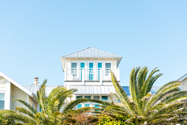 Modern beach house with white balcony and palm trees in front, representing vacation rentals on Florida’s Space Coast.