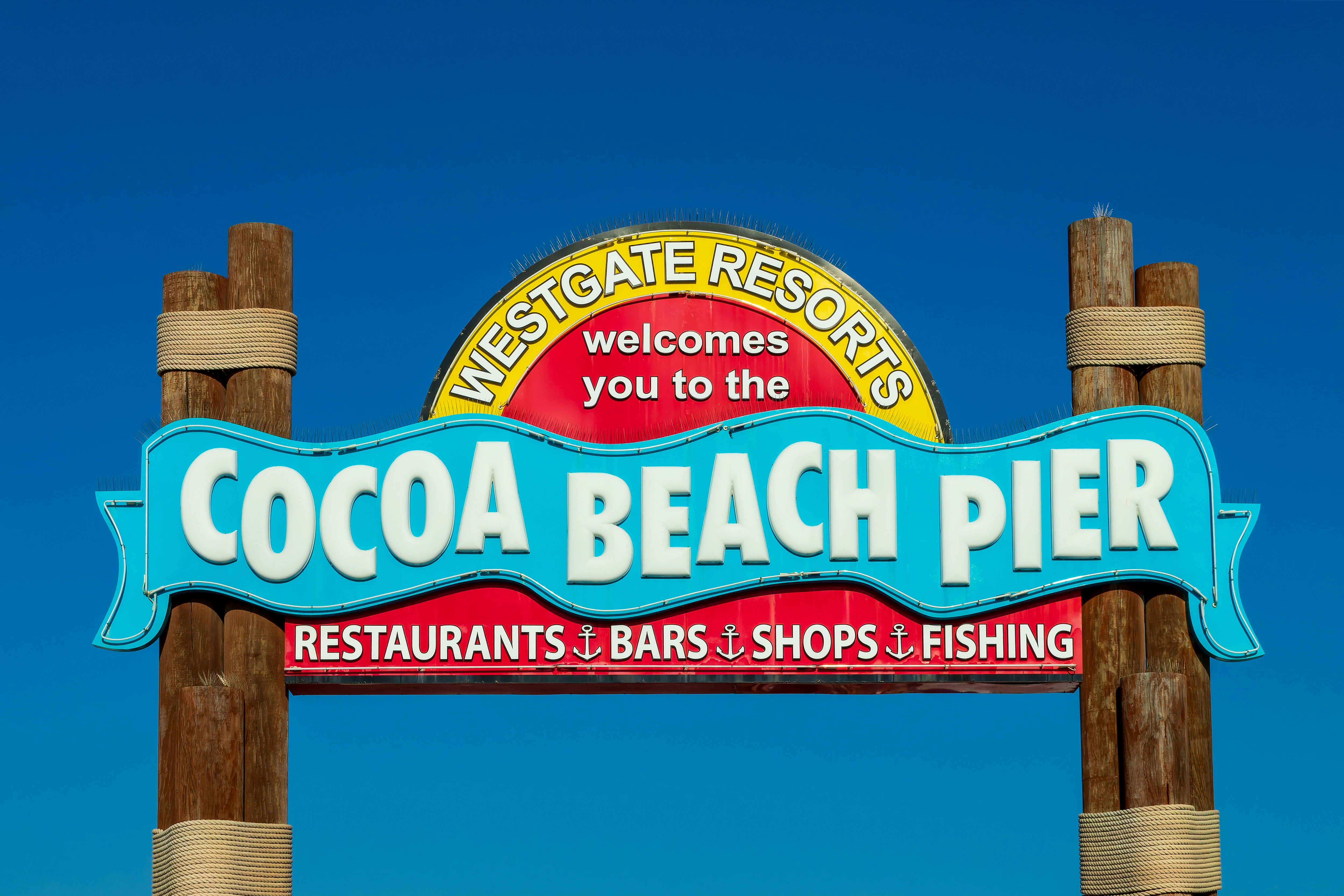 Colorful entrance sign for Cocoa Beach Pier in Florida, featuring restaurants, bars, shops, and fishing attractions.