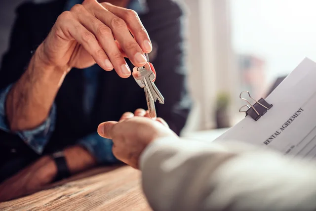Landlord handing over house keys with signed rental agreement.