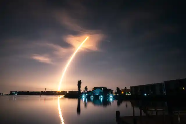 Nighttime rocket launch over Florida’s Space Coast reflecting on calm water near residential properties in Brevard County.